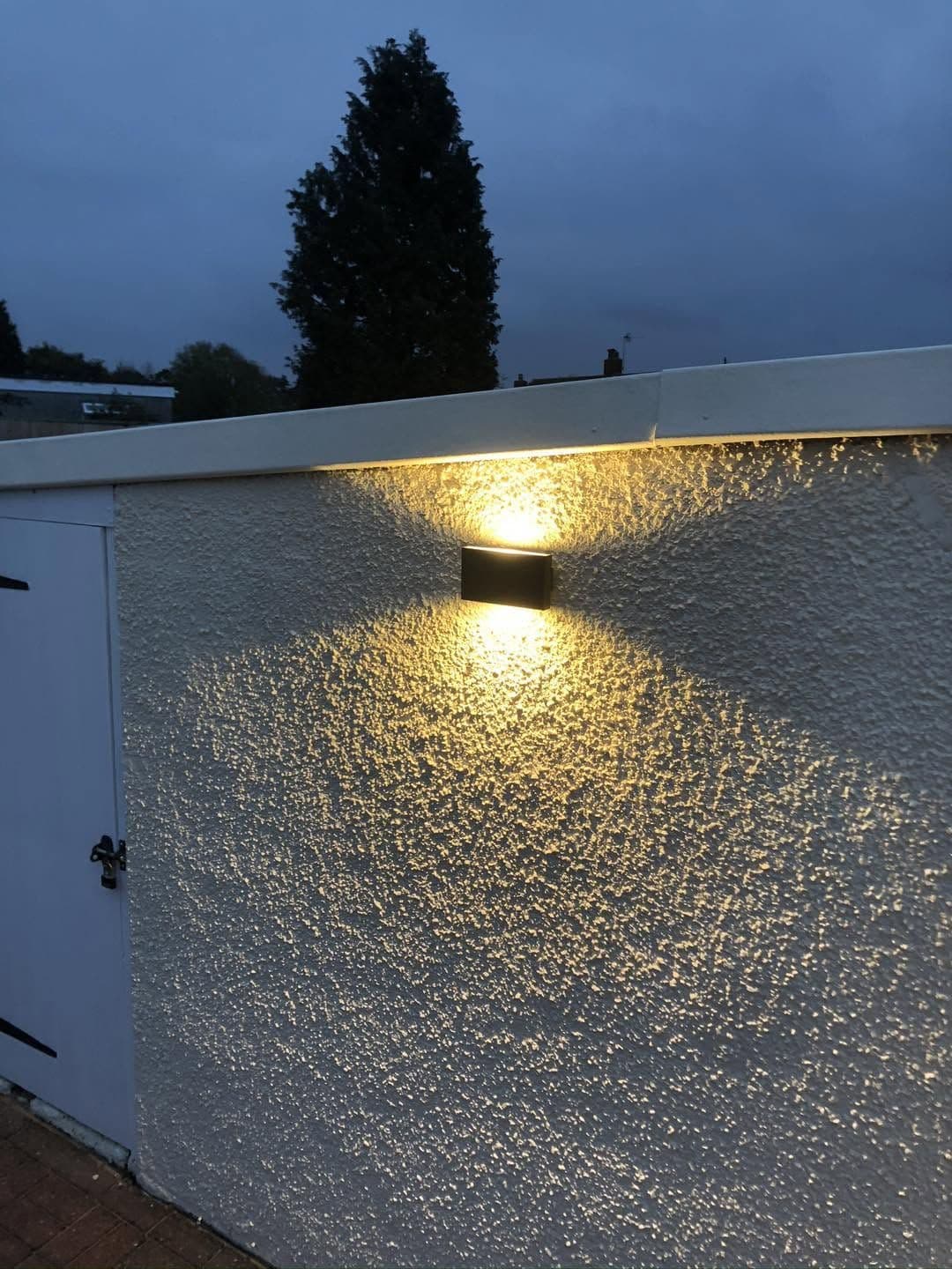 Wall light fitted to a rendered garage, lit at dusk