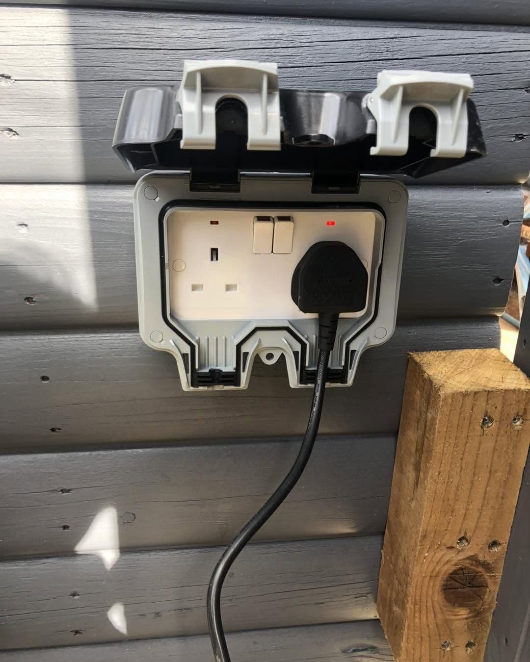 Weatherproof outdoor socket and plug fitted to garden cladding